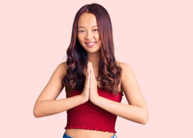 Genç, güzel Çinli bir kız, günlük giysiler içinde elleriyle dua ediyor, af diliyor, kendinden emin bir şekilde gülümsüyor.. 