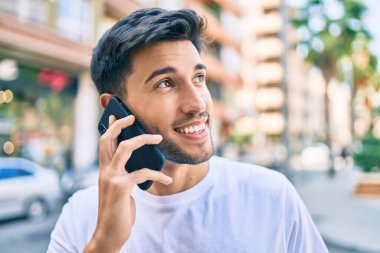 Genç Latin adam gülümsüyor ve şehirde akıllı telefondan konuşuyor..