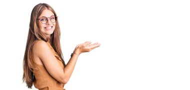 Gündelik kıyafetler ve gözlük takan genç güzel sarışın kadın avuçlarını açıp fotokopi alanını gösteriyor, gülümseyerek mutlu bir şekilde gülümsüyor. 