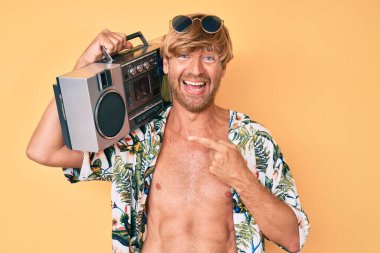 Sarışın, yaz tarzı giyinen genç bir adam, elinde kasetçalar, kahkahalarla gülüyor.. 