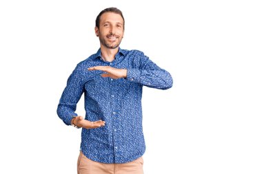 Elleriyle el kol hareketi yapan, büyük ve büyük beden işareti gösteren sıradan kıyafetler giyen genç yakışıklı bir adam. Kameraya bakıp gülümsüyor. ölçüm kavramı. 