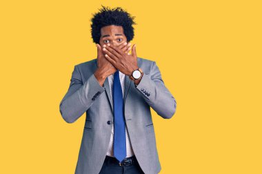 İş ceketi giyen afro saçlı yakışıklı Afro-Amerikan adam ağzını yanlışlıkla ellerle kapatmış. gizli kavram. 