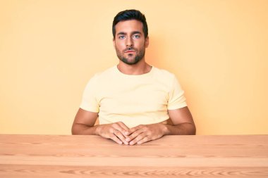 Masada oturan ve yüzünde ciddi bir ifadeyle gündelik giysiler giyen İspanyol bir genç. Basit ve doğal bir şekilde kameraya bakıyorsun.. 