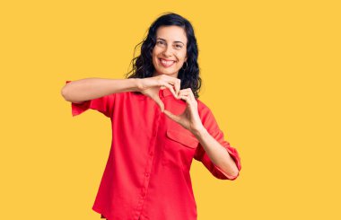 Gündelik kıyafetler giyen, aşık gülümseyen, elleriyle kalp sembolü yapan genç, güzel İspanyol bir kadın. romantik kavram. 