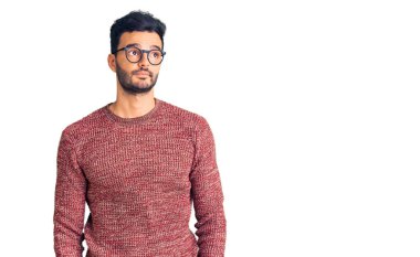 Genç, yakışıklı, süveter ve gözlük takan yakışıklı bir adam gülümseyip yan tarafa bakıyor ve düşünüyor.. 