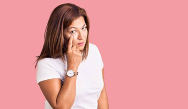 Orta yaşlı, beyaz tişört giyen Latin bir kadın senin jestini ve şüpheli ifadeni izliyor. 