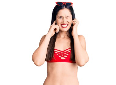 Bikini giyen beyaz bir kadın yüksek sesli müzik sesi için kulaklarını parmaklarıyla kapatıyor. sağır kavramı. 