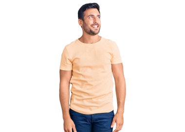 Gündelik kıyafetler giyen genç İspanyol bir adam yüzünde gülümsemeyle yan yana bakıyor, doğal bir ifade. Kendinden emin gülen. 