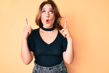 Gündelik giysiler giyen genç, beyaz bir kadın şaşkın şaşkın yukarı bakıyor ve parmaklarıyla işaret ediyor ve kollarını kaldırıyordu.. 