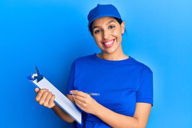 Güzel esmer kadın kurye üniforması giyiyor elinde dosyayla mutlu ve havalı bir gülümsemeyle gülümsüyor. diş gösterme. 