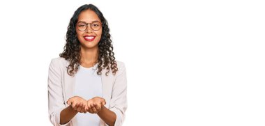 İş kıyafetleri giymiş, elleri avuçlarında gülümseyen, el hareketi yapan Afro-Amerikalı genç bir kız. Bekleme ve koruma 