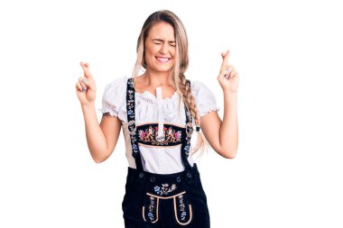 Oktoberfest elbisesi giyen genç güzel sarışın kadın umut ve gözlerin kapalı bir şekilde gülümseyerek işaret ediyor. Şans ve batıl inançlar. 