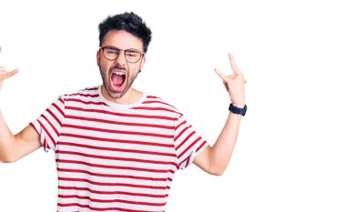 Latin asıllı genç adam, gündelik kıyafetler giyip çılgın bir ifadeyle bağırıyor ve elleri havada rock sembolü yapıyor. Müzik yıldızı. ağır müzik konsepti. 