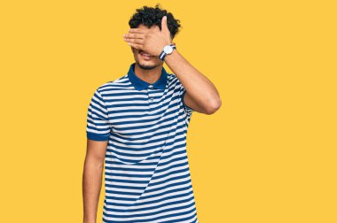 Gündelik giysiler ve gözlük takan genç bir Arap. Gülümsüyor ve elleri yüzünde, şaşırtmak için gözleri kapatıyordu. kör kavram. 