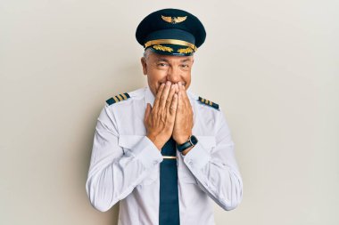 Yakışıklı, orta yaşlı, uçak pilotu üniforması giyen, gülen ve utanan, ağzı ellerle, dedikoduyla ve skandal konseptiyle örten olgun bir adam. 