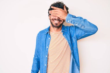 Kıvırcık saçlı ve ayı gibi sıradan bir kot ceket giyen yakışıklı genç adam. Gülümseyen ve gülen elleri yüzüyle şaşırtmak için gözlerini kapatıyor. kör kavram. 