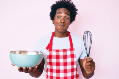 Afro saç pişiren yakışıklı Afro-Amerikalı adam fırıncı çırpıcı ve komik yüzlü yanaklar kullanıyor. Ağzı havayla şişer, havayı yakalar.. 