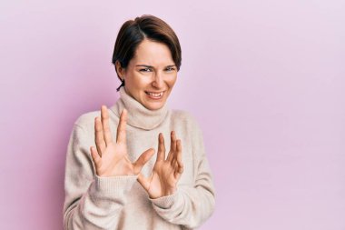 Kısa saçlı, kısa saçlı, kışlık süveter giyen genç esmer kadın tiksindirici ve tiksindirici bir ifade takınıyor çünkü tiksinti tepki veriyor. Eller havada. 