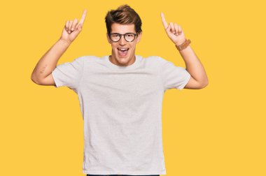 Yakışıklı, günlük kıyafetler ve gözlük takan beyaz bir adam. Şaşırmış, şaşırmış, parmaklarıyla işaret ediyor ve kollarını kaldırıyordu.. 