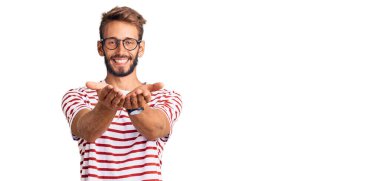 Sarışın, sakallı, sıradan kıyafetler giyen ve elleri avuçlarında gülümseyen, el hareketi yapan yakışıklı bir adam. Bekleme ve koruma 