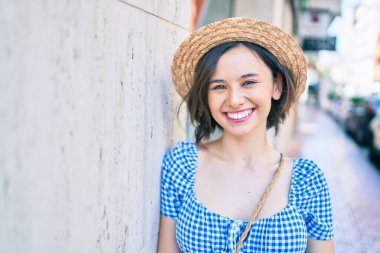 Genç ve güzel bir kız gülümsüyor. Mutlu bir şekilde şehrin duvarına yaslanıyor.