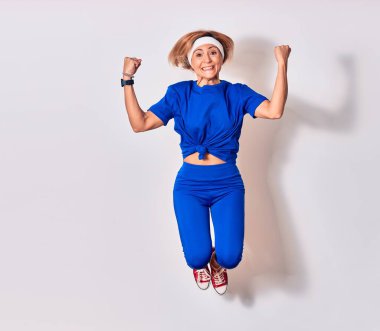 Genç beyaz kadın spor giyer, mutlu bir şekilde gülümser. Yüzünde tebessümle zıpla kazanan imzayı at yumruklarınla yalıtılmış beyaz arka planda