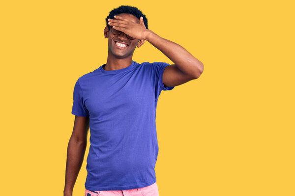 African handsome man wearing casual clothes and glasses smiling and laughing with hand on face covering eyes for surprise. blind concept.