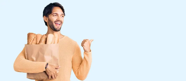 Bonito Hispânico Homem Segurando Saco Papel Com Pão Apontando Polegar — Fotografia de Stock