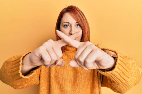 漂亮的红头发女人 穿着休闲的冬季毛衣 披着黄色背景的排斥表情 交叉着手指做着阴性手势 — 图库照片