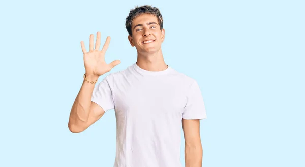 若いですハンサムな男身に着けていますカジュアルな白いTシャツ表示し 指番号5で指摘しながら笑顔自信と幸せ — ストック写真