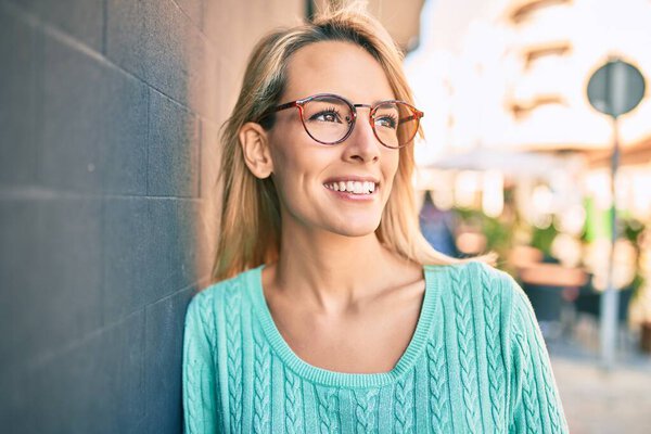 Молодая блондинка улыбается счастливая, прислонившись к стене города.