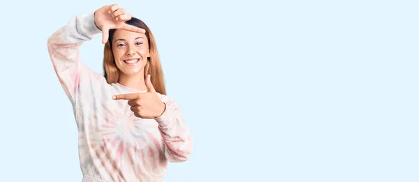 カジュアルなタイ染料のスウェットシャツを着た美しい若い女性は 幸せな顔で手や指でフレームを作り笑顔 創造性と写真の概念 — ストック写真