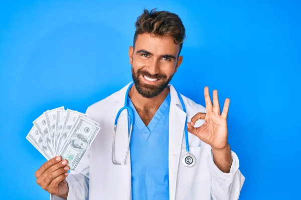 Joven Hombre Hispano Vistiendo Uniforme Médico Sosteniendo Dólares Haciendo Señal — Foto de Stock