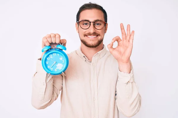 Joven Hombre Guapo Sosteniendo Despertador Haciendo Señal Con Los Dedos — Foto de Stock