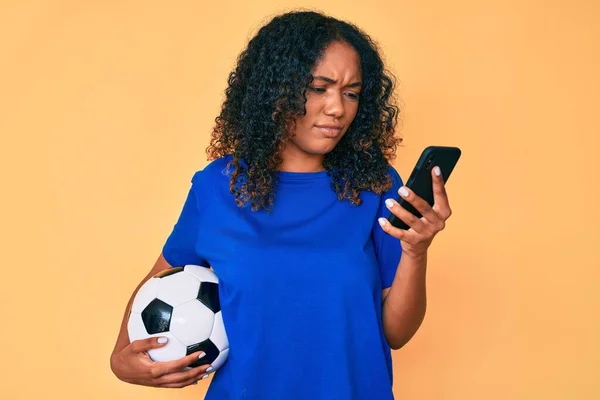 Jovem Afro Americana Segurando Bola Futebol Olhando Para Smartphone Cético — Fotografia de Stock