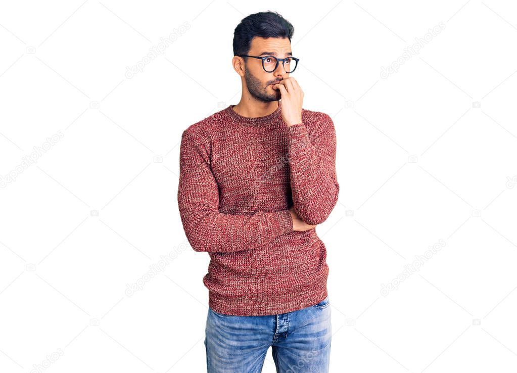 Young handsome hispanic man wearing winter sweater and glasses looking stressed and nervous with hands on mouth biting nails. anxiety problem. 