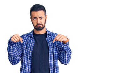 Gündelik kıyafetler giyen genç İspanyol adam üzgün ve üzgün görünüyor, parmaklarıyla yön gösteriyor, mutsuz ve depresif.. 