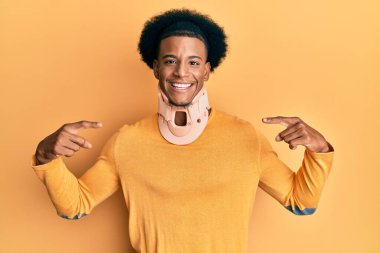 Afro saçlı, boyun yakalı, kendine güvenen, yüzünde gülümseme olan, kendini gururlu ve mutlu parmaklarıyla gösteren Afro-Amerikan bir adam.. 