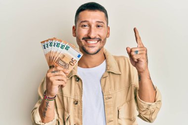 50 Euro 'luk banknotları olan yakışıklı bir adam bir fikir veya soruyla gülümsüyor ve mutlu bir yüzle işaret ediyor. 