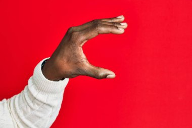 Afro-Amerikan siyahi bir gencin eli ve kolu, kırmızı izole edilmiş arka plan üzerinde. Görünmez bir şeyi alıyor, parmaklarıyla uzayı gösteren bir nesneyi tutuyor. 