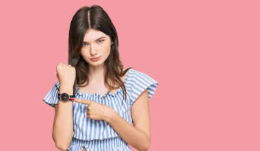 Genç, beyaz, günlük kıyafetler giymiş genç bir kız saati, sabırsızlığı ve rahat bir ifadeyle kameraya bakıyor. 