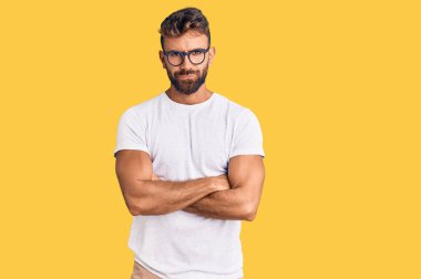 Gündelik kıyafetler giyen, gözlüklü, şüpheci ve gergin genç İspanyol bir adam. Yüzünde çapraz kollarla onaylamayan bir ifade var. negatif kişi. 