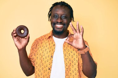 Örgülü genç Afro-Amerikan adam parmaklarıyla imza atıyor, gülümseyerek mükemmel bir sembol oluşturuyor. 