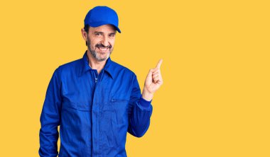 Yüzünde kocaman bir gülümseme olan, orta yaşlı, yakışıklı bir adam kameraya el ile işaret ediyor.. 