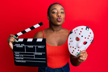 Genç Afrikalı Amerikalı kadın elinde video film klasörü ve korku maskesiyle kameraya bakıp öpüşürken çok güzel ve seksi görünüyor. aşk ifadesi. 