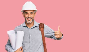 Güvenlik kaskı takan, elinde planlar tutan, mutlu ve olumlu gülümseyen orta yaşlı, kır saçlı bir adam. 