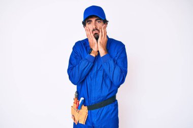 Handsome young man with curly hair and bear weaing handyman uniform tired hands covering face, depression and sadness, upset and irritated for problem 