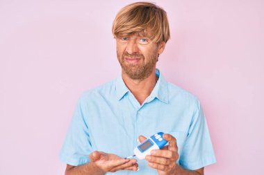 Genç sarışın adam glikoz ölçer kullanıyor. Bilgisi yok ve kafası karışık. şüphe kavramı. 