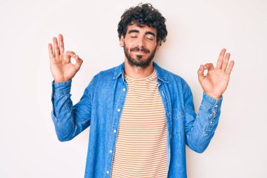 Kıvırcık saçlı yakışıklı genç adam ve sıradan kot ceket giyen ayı rahatla ve gözleri kapalı gülümse parmaklarıyla meditasyon hareketi yapıyor. yoga konsepti. 