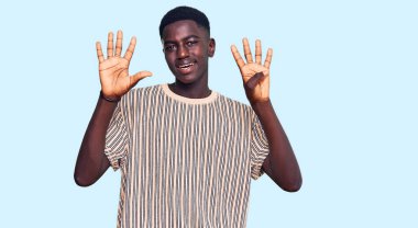 Genç, Afro-Amerikalı, günlük kıyafetler giymiş, dokuz numaralı parmaklarıyla işaret ederken, kendinden emin ve mutlu bir şekilde gülümsüyor.. 